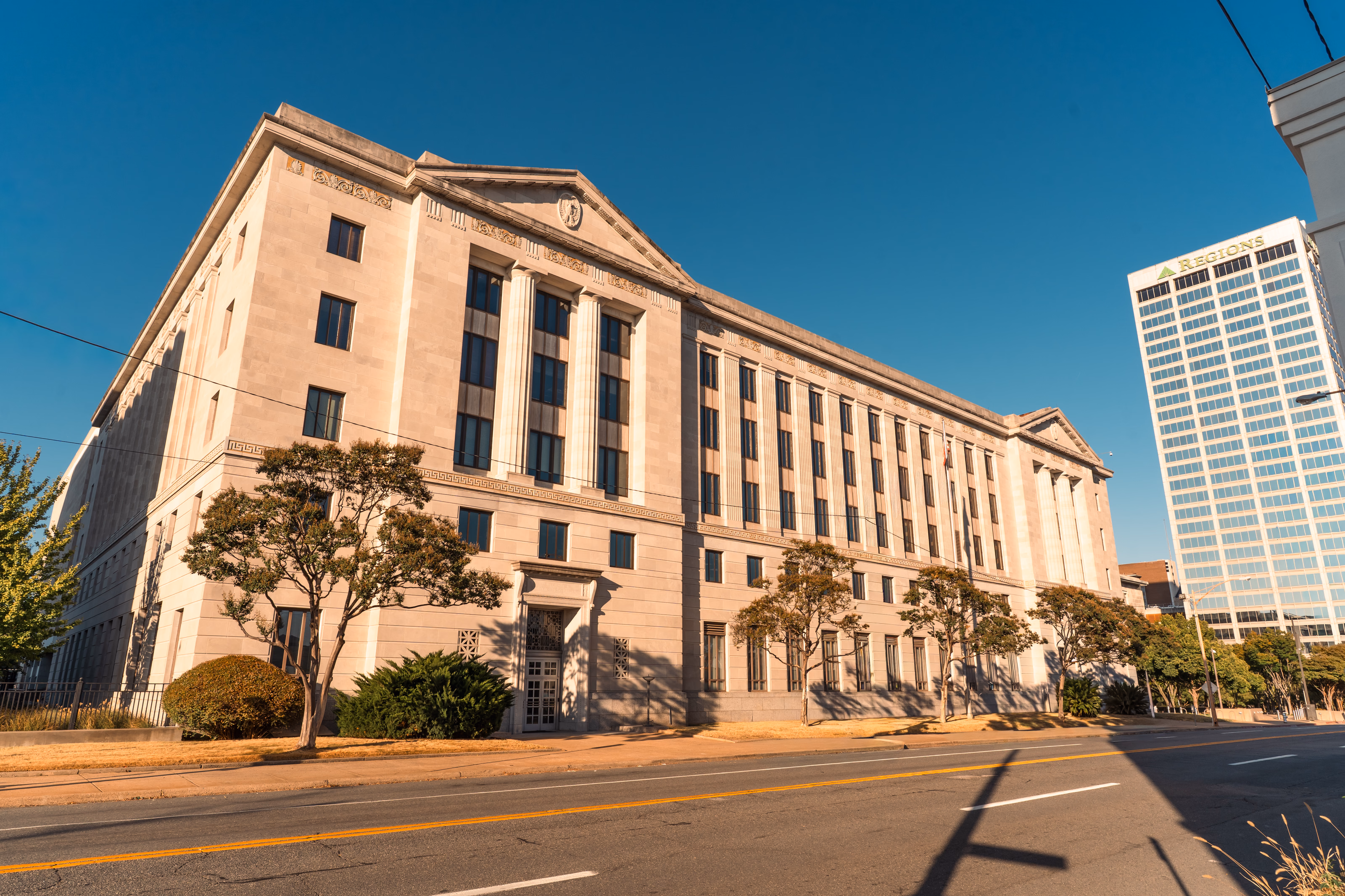 A limestone courthouse front, fluted pilasters rising to a carved pediment, in low sun